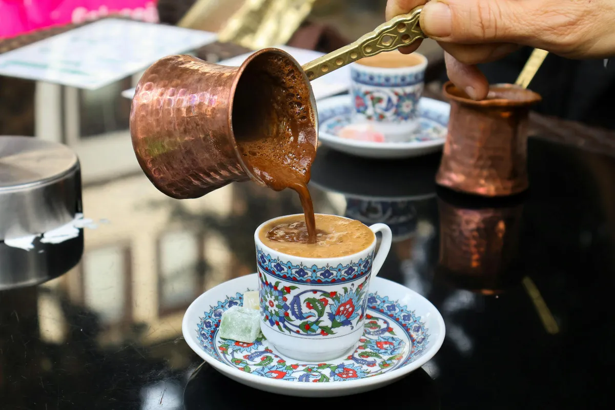 Café turc versé depuis un cezve en cuivre dans une tasse en porcelaine d'Iznik avec lokum, rituel UNESCO