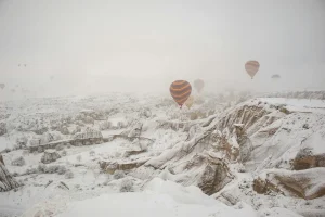 Cheminees de fee de Cappadoce couvertes de neige avec montgolfieres dans le ciel brumeux d'hiver