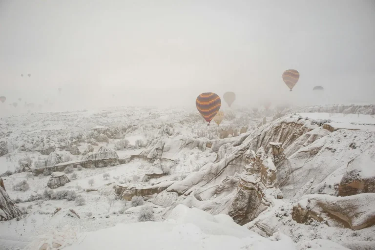 Cheminees de fee de Cappadoce couvertes de neige avec montgolfieres dans le ciel brumeux d'hiver
