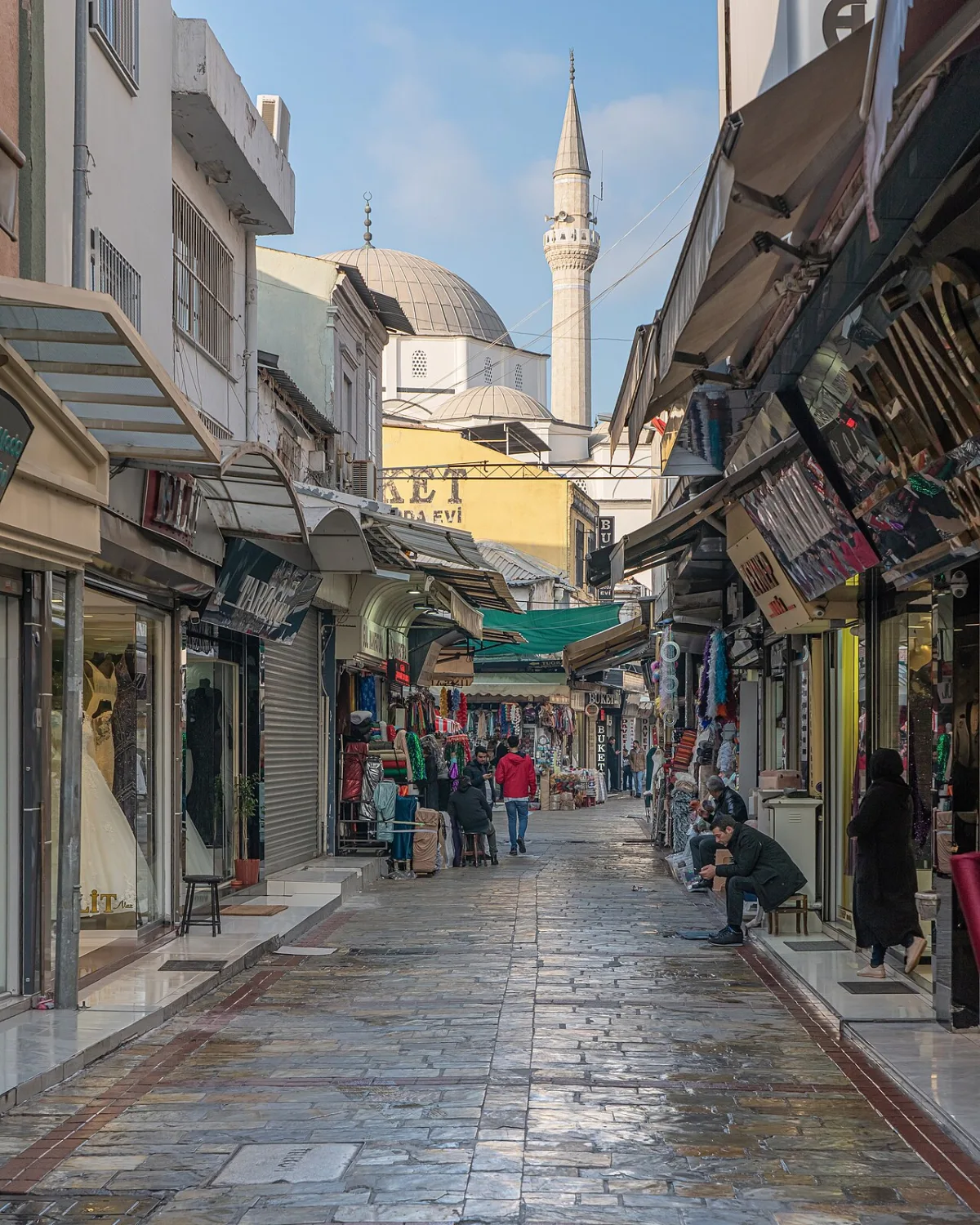 Ruelle commercante étroite bordée d'echoppes, dome et minaret d'une mosquee au fond
