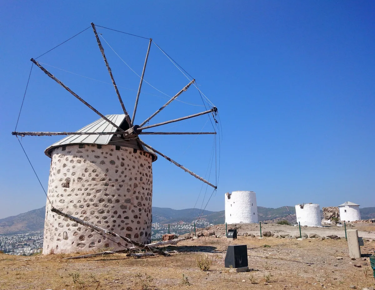 Moulin à vent en pierre chaulée aux ailes de bois, trois autres tours en ruine alignées sur une crête aride