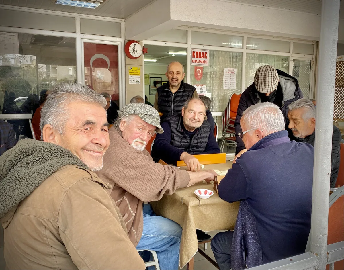 Hommes âgés attablés autour d'une partie de tuiles sous l'auvent d'un café de quartier