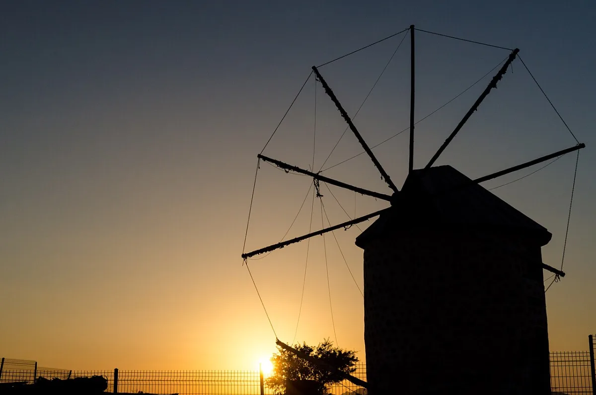 Silhouette d'un moulin à vent en pierre à ailes de bois devant un ciel orange