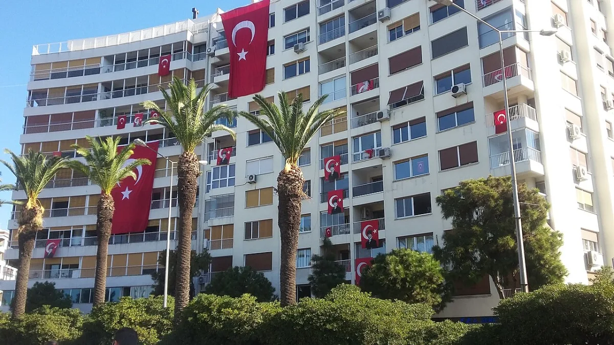 Drapeaux turcs et portraits d'Atatürk suspendus aux balcons d'un immeuble bordé de palmiers à İzmir