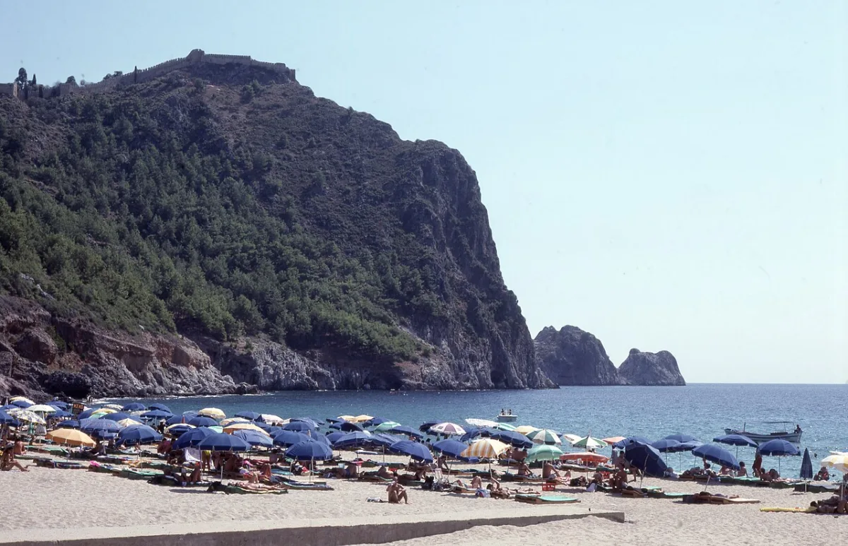 Plage de sable couverte de parasols et de baigneurs au pied du promontoire fortifié d'Alanya