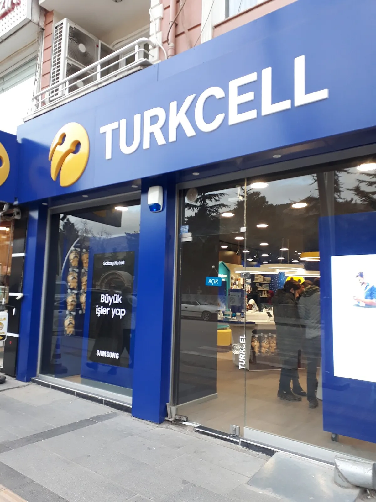 Devanture bleue d'une boutique Turkcell au pied d'un immeuble, logo jaune et affiche en turc en vitrine