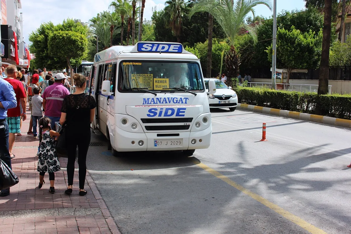 Minibus dolmuş blanc et bleu de la ligne Manavgat-Side arrêté le long d'un trottoir, passagers à côté